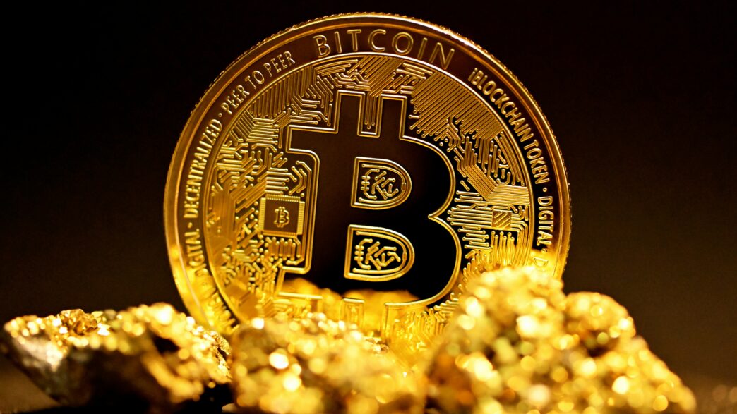 A single bitcoin surrounded by raw gold pieces.