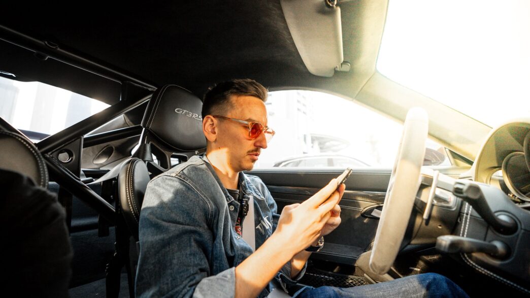 Carl Moon, crypto investor and racing driver, sitting in a sports car checking his phone